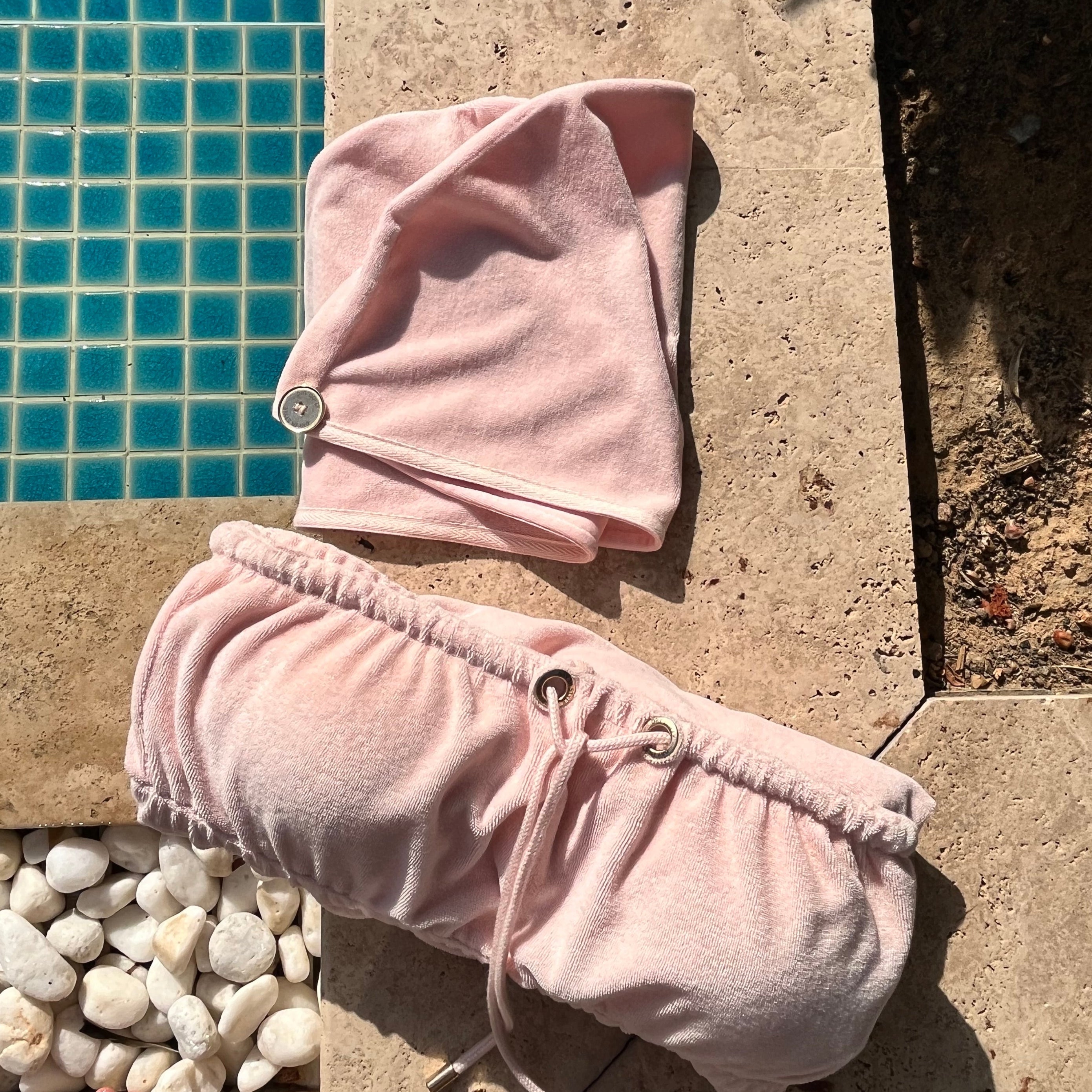 Folded Dry Dolly towel dress with matching head towel placed by a poolside, showcasing stylish and practical post-shower essentials