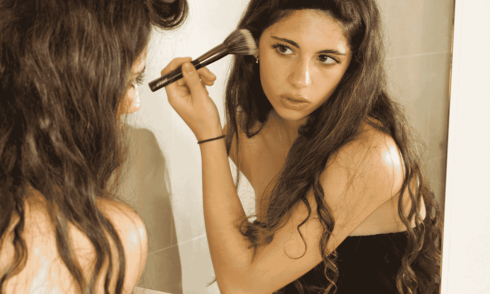 Woman wearing a Dry Dolly stylish towel dress while doing her hair and makeup in the bathroom.
